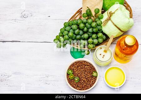 Accessoires de spa naturels et raisins verts. Des ingrédients frais pour des soins personnels sains et confortables. Arrière-plan en bois blanc, vue du dessus Banque D'Images