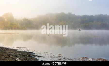 Paysage d'automne avec un pêcheur sur le lac dans le brouillard. Tôt le matin sur le lac. Un pêcheur solitaire dans un bateau. Un brouillard épais et gris le matin. Détente Banque D'Images