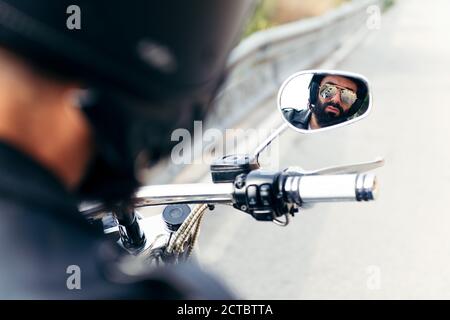 biker avec casque et lunettes de soleil se reflète dans le miroir de sa moto, concept de liberté et style de vie rebelle Banque D'Images