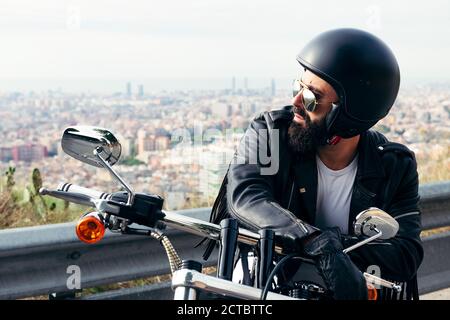 biker avec casque et veste en cuir assis sur sa moto avec la ville en arrière-plan, concept de liberté et de style de vie rebelle, copie spac Banque D'Images