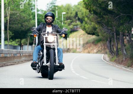 biker avec casque, lunettes de soleil et veste de cuir de sa moto sur la route, concept de liberté et de style de vie rebelle Banque D'Images
