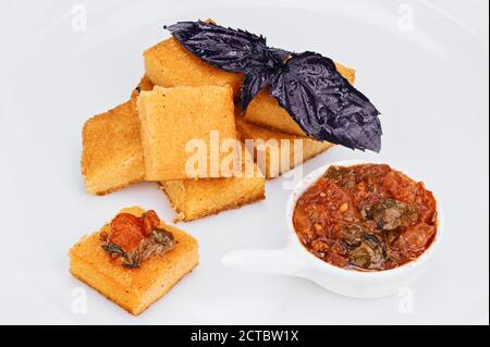 Tranches de farine de maïs italienne traditionnelle repas vegan polento cuit avec légumes frits et feuilles de basilic foncé isolées sur blanc Banque D'Images