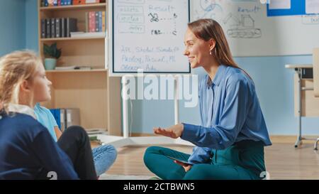 Classe de créativité scolaire: Les enfants assis sur le tapis tout en aidant le professeur explique la leçon en utilisant la tablette numérique ordinateur. Enfants intelligents Banque D'Images