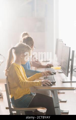 Photo verticale dans l'école élémentaire informatique en classe: Rangées de divers petits élèves intelligents utilisant des ordinateurs personnels, apprendre l'informatique Banque D'Images