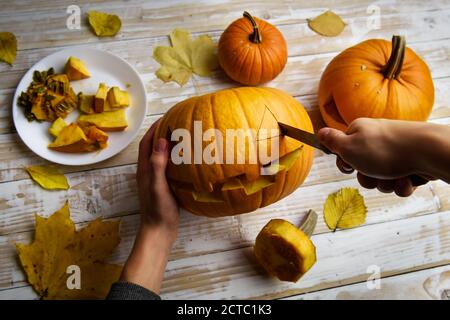 Sculpture Halloween. Gros plan sur les mains des enfants avec citrouille ou citrouille-lanterne et couteau à la maison. Décoration et concept de vacances Banque D'Images