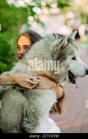 Une jeune femme atteinte de désordre inné nanisme embrasse le chien malamute tout en marchant dans le parc. Banque D'Images