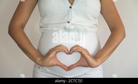 Femme enceinte portant un pantalon de maternité et formant un cœur sur son estomac. Banque D'Images