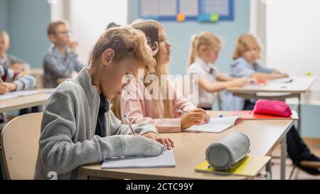 Salle de classe élémentaire de divers enfants écoutant attentivement leur leçon de professeur. Brillant jeunes enfants à l'école écrire dans l'exercice Banque D'Images