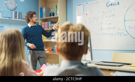 Le professeur explique la leçon à une salle de classe pleine de lumière divers enfants, montre les formules scientifiques et les données sur le tableau blanc. À l'école primaire Banque D'Images