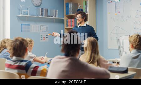 Un professeur enthousiaste explique la leçon à une salle de classe pleine de lumière divers enfants, enseigne la géométrie, les mathématiques. Dans le groupe d'école élémentaire de Bright Banque D'Images