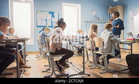 Un professeur enthousiaste explique la leçon à une salle de classe pleine de divers enfants. Dans l'école élémentaire Groupe de Smart multiethnique enfants écrire dans l'exercice Banque D'Images