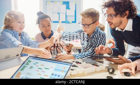 École primaire robotique salle de classe: Groupe diversifié d'enfants brillants avec enseignant enthousiaste de construction et de programmation robot. Apprentissage des enfants Banque D'Images