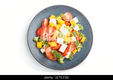 Salade végétarienne au brocoli, tomates, feta et potiron sur une assiette en céramique bleue isolée sur fond blanc, vue de dessus, gros plan. Banque D'Images