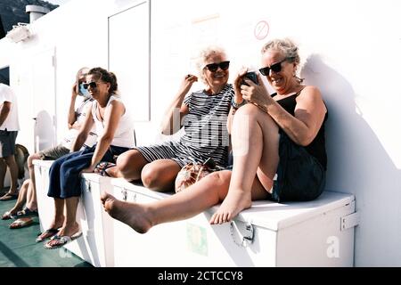 Les femmes âgées se trouvent sur un ferry en Croatie. Ils sourient et tapent sur d'autres smartphones. Banque D'Images