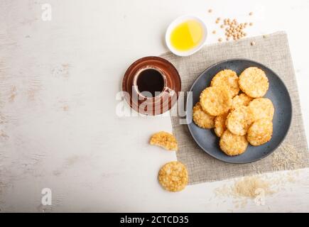 Le riz japonais traditionnel croustilles biscuits avec du miel et de la sauce soja sur une assiette en céramique bleue et une tasse de café sur fond blanc en bois. Vue de dessus, f Banque D'Images