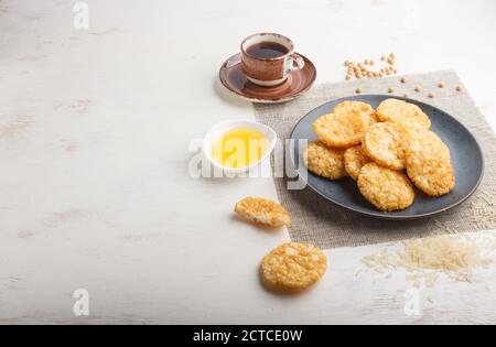 Biscuits japonais traditionnels aux chips de riz avec sauce au miel et au soja sur une assiette en céramique bleue et une tasse de café sur fond de bois blanc. Vue latérale, Banque D'Images