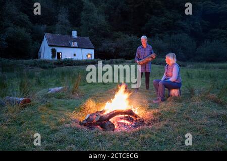 Deux femmes se sont rassemblées autour de feu de joie avec chalet en arrière-plan en automne, Exmoor, Somerset, Angleterre, Royaume-Uni, Europe Banque D'Images