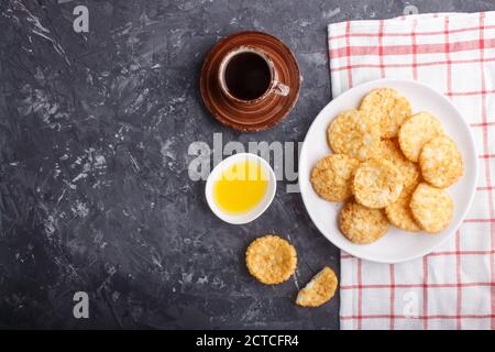 Le riz japonais traditionnel croustilles biscuits avec du miel et de la sauce soja sur une plaque en céramique blanche et une tasse de café sur fond de béton noir. Vue de dessus Banque D'Images