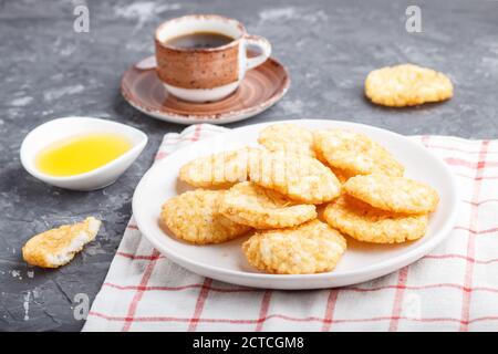 Le riz japonais traditionnel croustilles biscuits avec du miel et de la sauce soja sur une plaque de céramique blanche et une tasse de café sur un fond de béton noir. Côté vie Banque D'Images