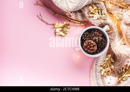 Cônes de pin dans une tasse émaillée grise, feuilles d'or, guirlande lumineuse et un plaid crocheté sur fond rose. Flat Lay, vue de dessus, automne, Thanksgiving Banque D'Images