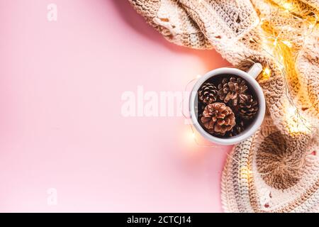 Cônes de pin dans une tasse émaillée grise, guirlande lumineuse et un plaid crocheté sur fond rose. Flat Lay, vue de dessus, automne, concept de Thanksgiving. Banque D'Images