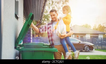 Père tenant une jeune fille et jetant un déchet de nourriture dans la corbeille. Ils utilisent des poubelles correctes car cette famille est de trier les déchets et Banque D'Images