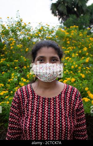 Belle dame avec masque floral, boucles d'oreilles et supports haut de gamme de designer avant les fleurs jaunes. Protection contre le corona avec élégance. Banque D'Images