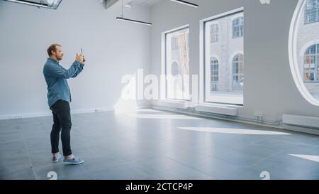 Jeune homme de taille basse dans des lunettes debout dans un bureau vide et de la mapper avec un logiciel de réalité augmentée sur une tablette. La lumière du soleil brille à travers les grandes fenêtres. Banque D'Images
