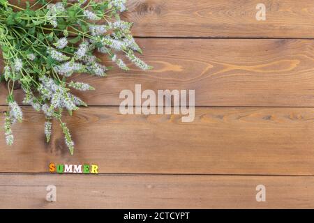 Un bouquet d'origan fleuri se trouve sur une table en bois marron. Été ensoleillé. Lettres multicolores. Copier l'espace Banque D'Images