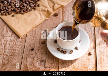 café fraîchement préparé dans la cafetière (cafetière turque traditionnelle) La main de la femme verse le café dans une tasse blanche Banque D'Images