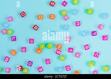 Perles cubes en plastique multicolore avec lettres éparpillées sur fond bleu. Texture d'arrière-plan de l'alphabet. Banque D'Images