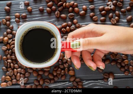 Main féminine tenant une tasse de café sur un fond de grains de café allongé sur la table, vue du dessus. Banque D'Images