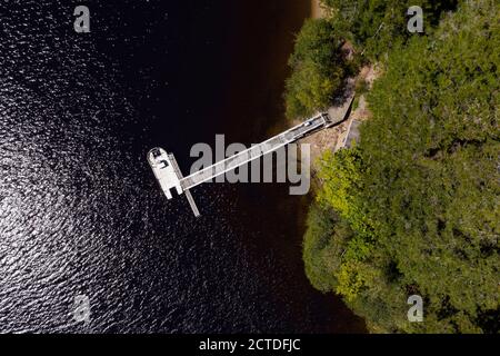 Vue aérienne de topview photo d'un quai privé avec un bateau à moteur sur la rive d'une île couverte de forêt éloignée. Banque D'Images