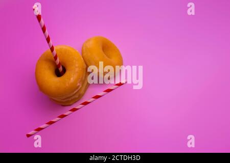 Trois Donuts ou classiques Donuts pile avec deux bandes rouges de paille sur un fond rose. Banque D'Images