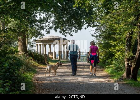 Couple marchant avec un chien dans une forêt approchant du Mémorial Inglis, un point de repère sur Colley Hill dans l'AONB de Surrey Hills, au Royaume-Uni Banque D'Images