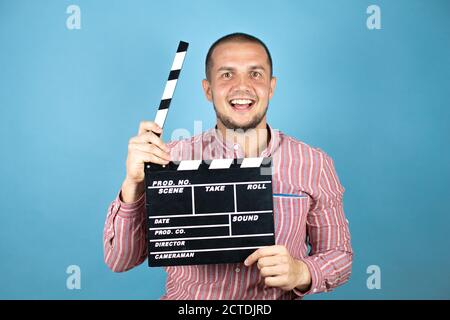 Homme d'affaires russe sur fond bleu tenant clapperboard très heureux amuse-toi bien Banque D'Images