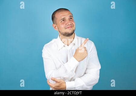 Homme d'affaires russe portant une chemise blanche sur fond bleu pointant le doigt vers le côté. Banque D'Images