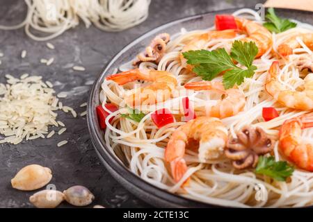 Nouilles de riz aux crevettes et petits pieuvres sur plaque en céramique grise sur fond de béton noir et textile orange. Vue latérale, gros plan, Banque D'Images