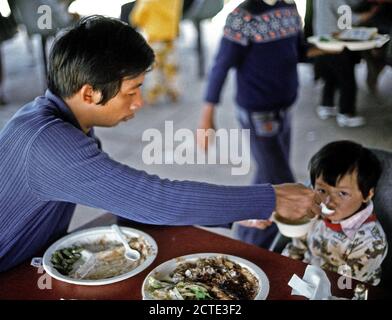 1975 - Un père nourrit ses enfants à un établissement de logements temporaires pour les réfugiés vietnamiens à Camp Pendleton, CA Banque D'Images