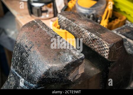 Gros plan de l'étau ou de l'étau à mâchoires. Arrière-plan de la table d'atelier de travail flou et doux avec têtes de vis, ruban de mesure et récipients jaunes. Banque D'Images