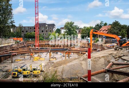 Fosse de fondation pour le chantier de construction d'un bâtiment résidentiel ou d'un parking. Tuyaux comme entretoises de la grande fosse, grue rouge, excavatrices jaune et orange. Banque D'Images