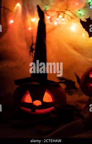 Halloween fête décoration citrouille sculptée dans la sorcière chapeau noir sinistre visage effrayant avec lumière dans une obscurité Banque D'Images