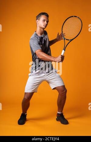 Portrait complet d'un joueur de tennis en action contre arrière-plan orange Banque D'Images