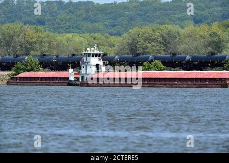Savane, Illinois, États-Unis. Un train de marchandises sur un lévee fluvial passe devant un bateau à remorqueurs parmi les barges sur le Mississippi. Banque D'Images