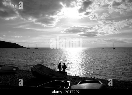 Un couple sur le front de mer de la plage de Totland Bay Isle of Le soir, le soleil couchant coucher de soleil derrière dans des yachts silhouette à ancrage dans la baie Banque D'Images