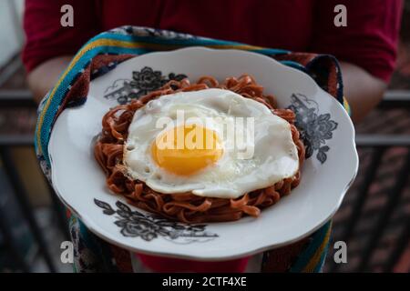 Les nouilles instantanées frites sont appréciées avec des œufs frits sur un Assiette avec un ornement en tissu typiquement indonésien Banque D'Images
