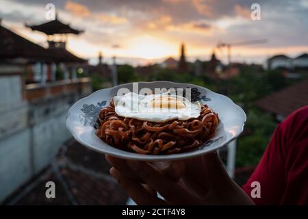 Les nouilles instantanées frites sont appréciées avec des œufs frits sur un Assiette avec un ornement en tissu typiquement indonésien Banque D'Images