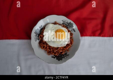 Les nouilles instantanées frites sont appréciées avec des œufs frits sur un Assiette avec un ornement en tissu typiquement indonésien Banque D'Images