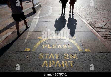 La face changeante de la rue haute. Les gens jettent des ombres à pied devant un panneau d'information social distancé peint sur le trottoir de la rue haute de Dundee en Écosse, environ six mois après la soirée du 23 mars lorsque le Premier ministre Boris Johnson a annoncé des restrictions à l'échelle nationale. Banque D'Images