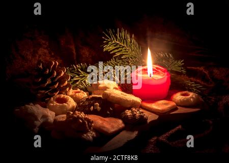 Bougie rouge allumée entre les biscuits de Noël décorés sur un panneau en bois devant un arrière-plan sombre Banque D'Images